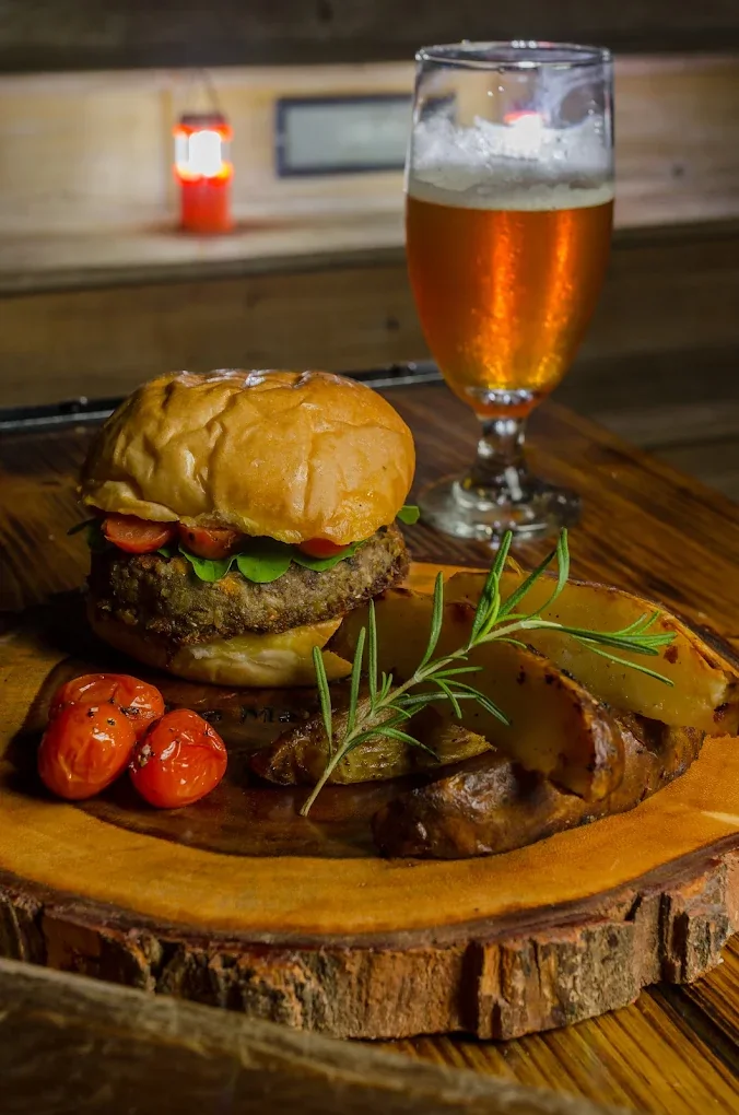 A burger with roasted potatoes and tomatoes beside a glass of beer