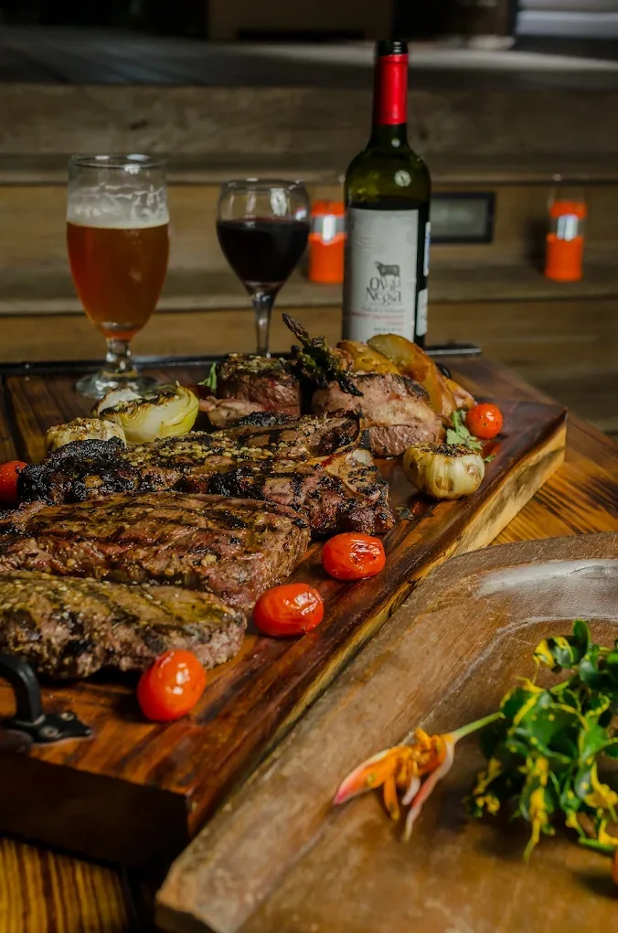 A board of grilled cuts with roasted onions, a glass of red wine and a beer