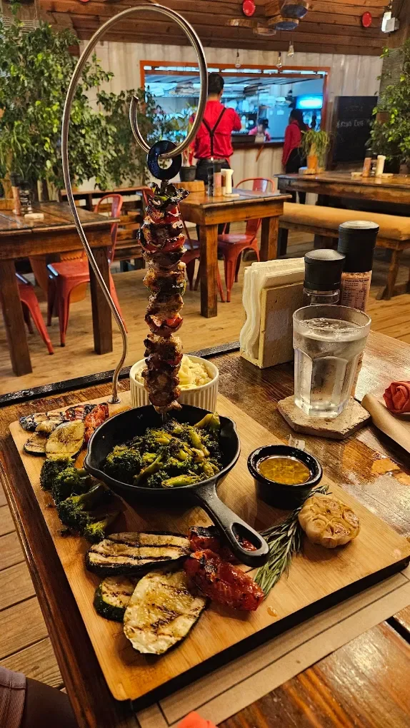 A hanging skewer over grilled vegetables, with the dining room behind