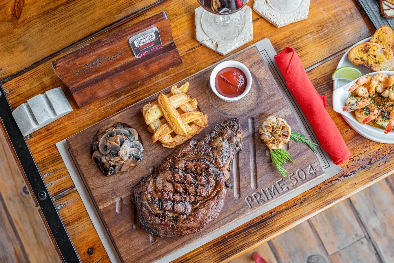 A grilled ribeye on a Prime 504 board with mushrooms, fries and roasted garlic