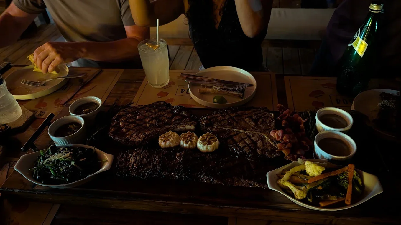 Three grilled steaks, roasted garlic and sides on a table at Prime 504